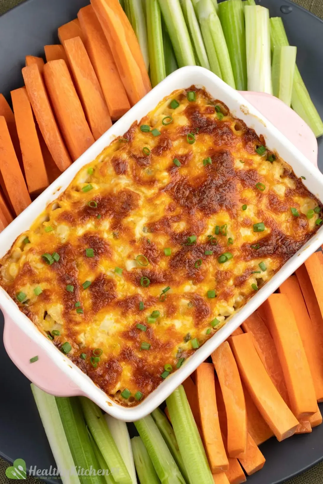 A ceramic baking pan filled with Buffalo Chicken Dip placed on a bed of celery sticks and carrot sticks