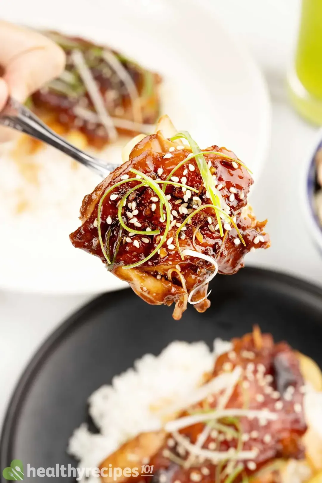 A spoon holding a piece of glossy grilled chicken hovering over a portion of cooked rice and teriyaki chicken