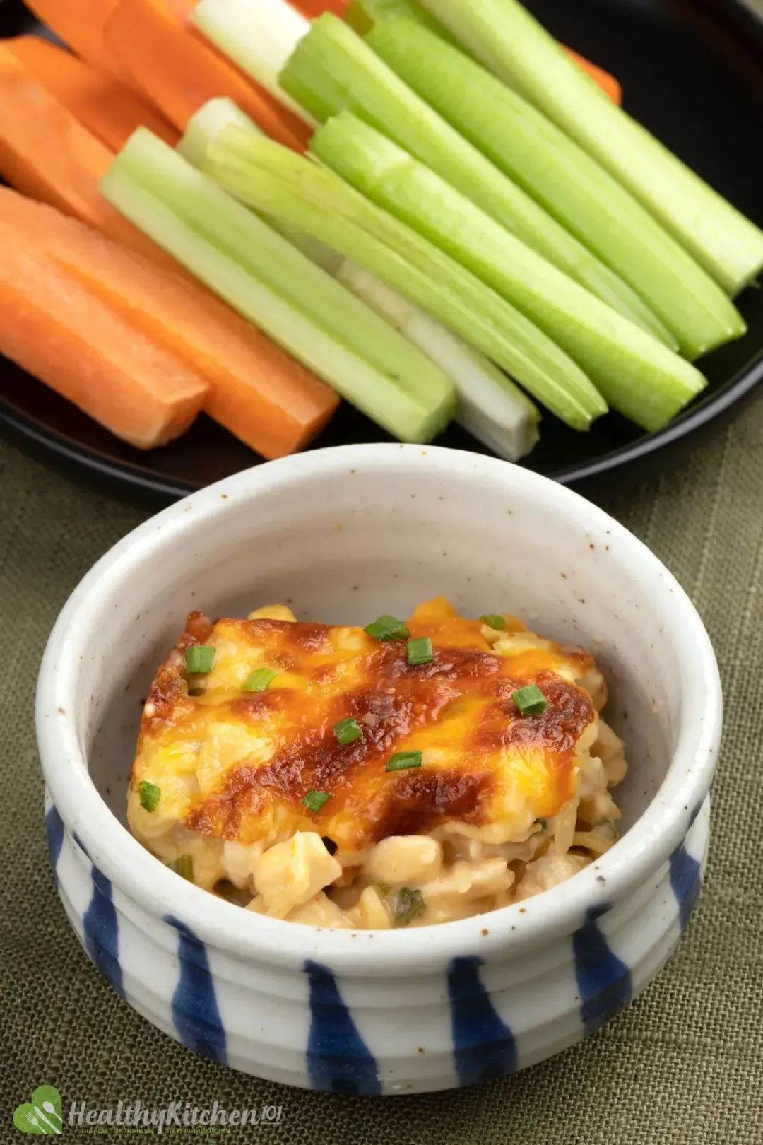 A small bowl of Buffalo Chicken Dip placed next to a plate of carrot sticks and celery sticks