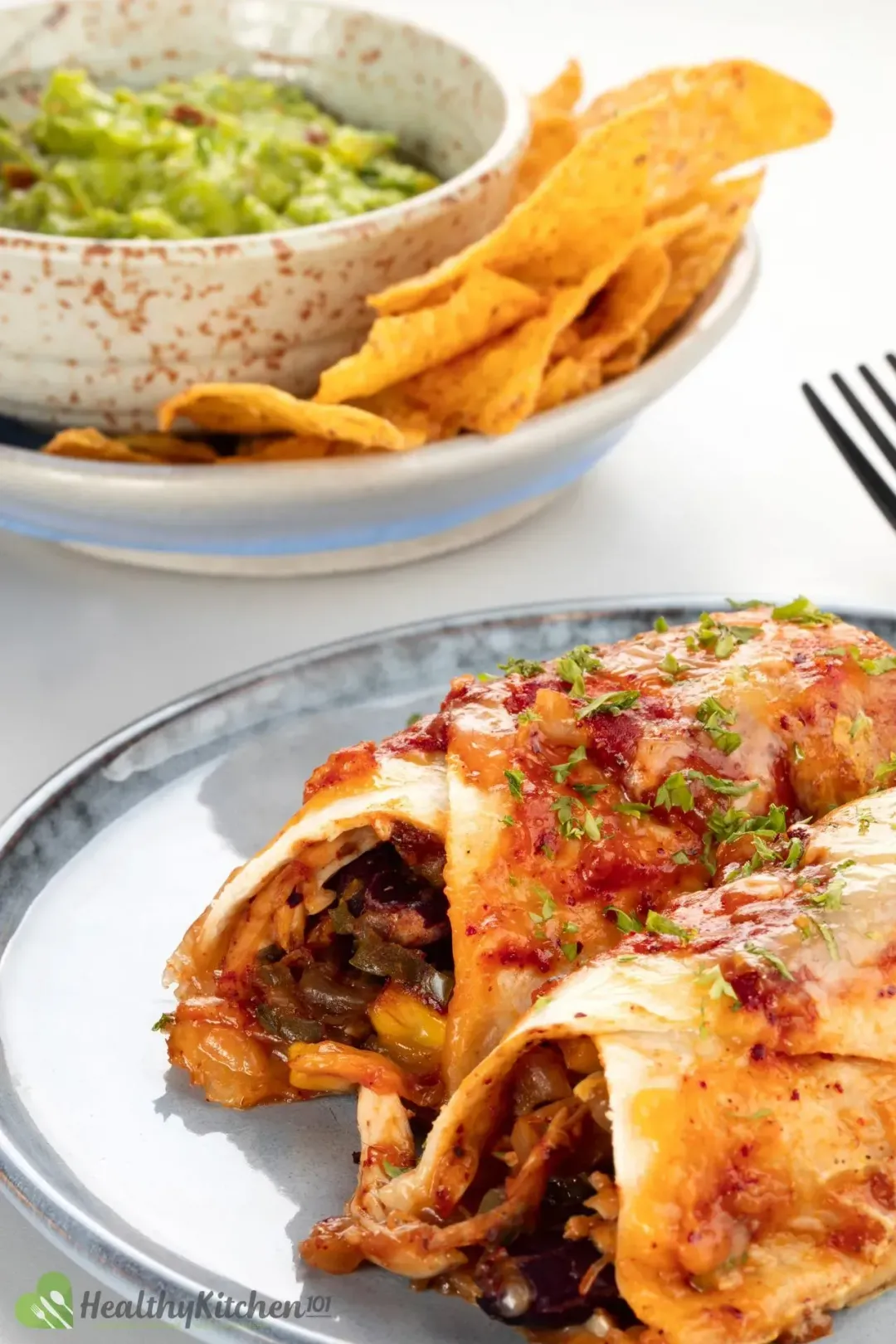 Two enchilada rolls on a blue-gray plate, next to tortillas and guacamole