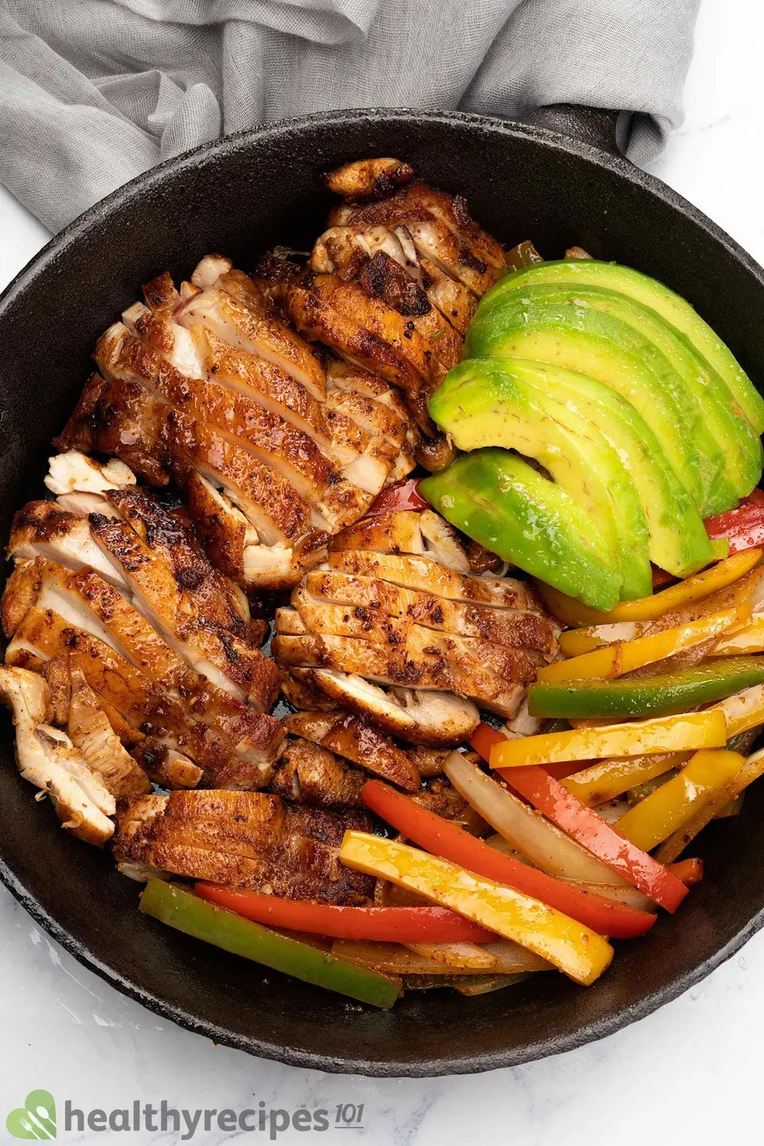 a cast iron skillet of cooked slices chicken with slices bell pepper and slices avocado