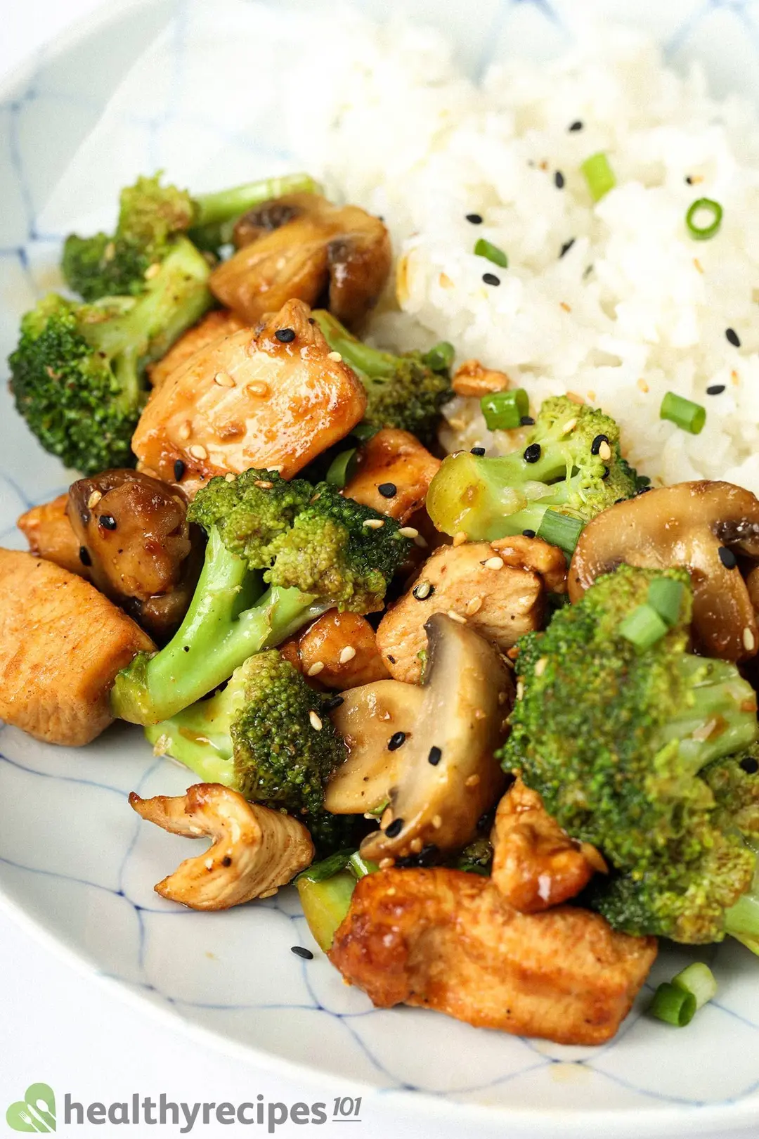 close-up shot of cooked cubed chicken with broccoli and mushroom serve with rice, garnished with sesame seeds and chopped scallion