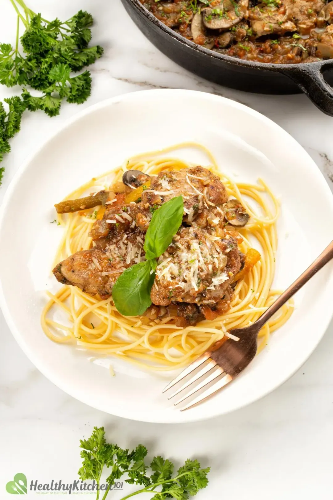 A plate of Chicken Cacciatore with a fork and some fresh herbs on the side.