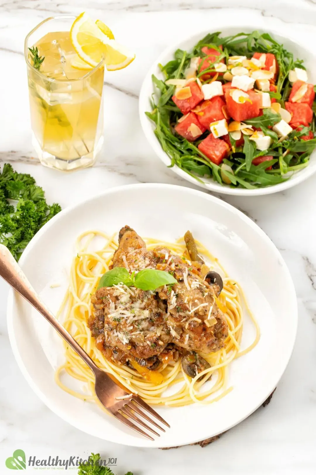 A meal consisting of a plate of Chicken Cacciatore, watermelon arugula salad, and a glass of lemon juice