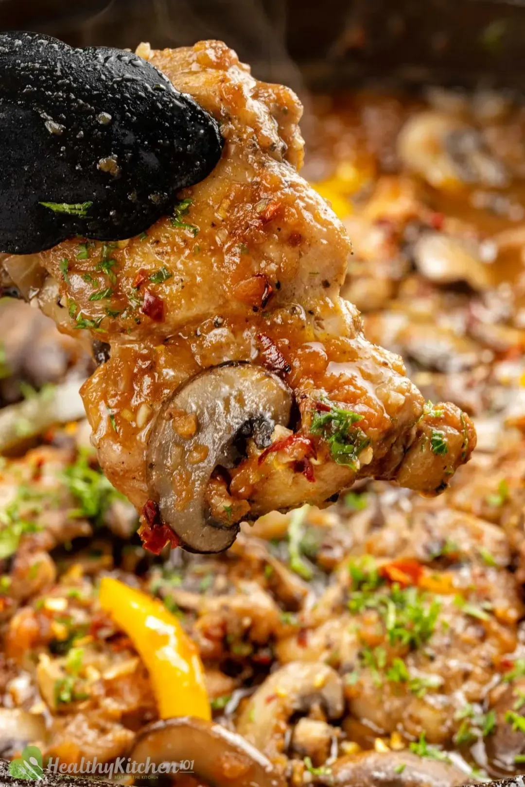 A pair of tongs picking up a piece of cooked chicken from a skillet of Chicken Cacciatore