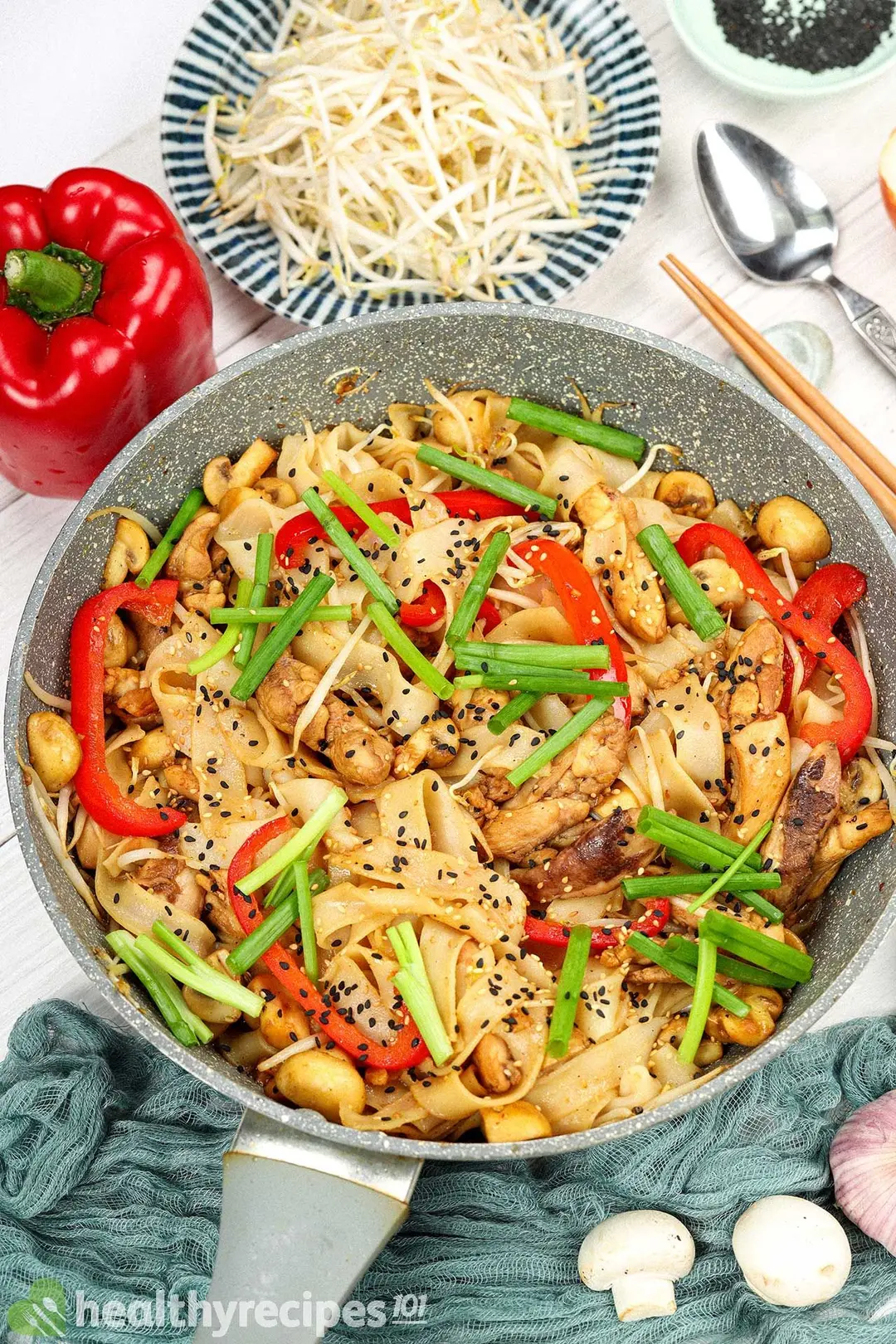Chicken chow fun with vegetables in a pan alongside raw peppers, mushrooms, and bean sprouts