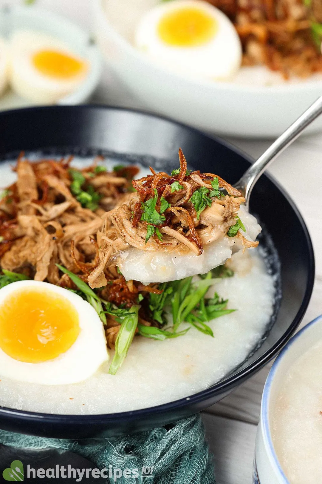 A close-up shot of a bowl of chicken congee with soft-boiled eggs, scallions, and cilantro