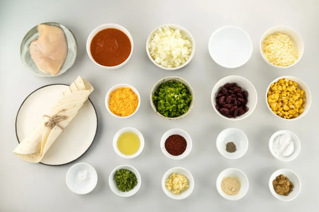 Ingredients: rolled-up tortillas, chicken breast, tomato sauce, vegetables, and spices in different bowls