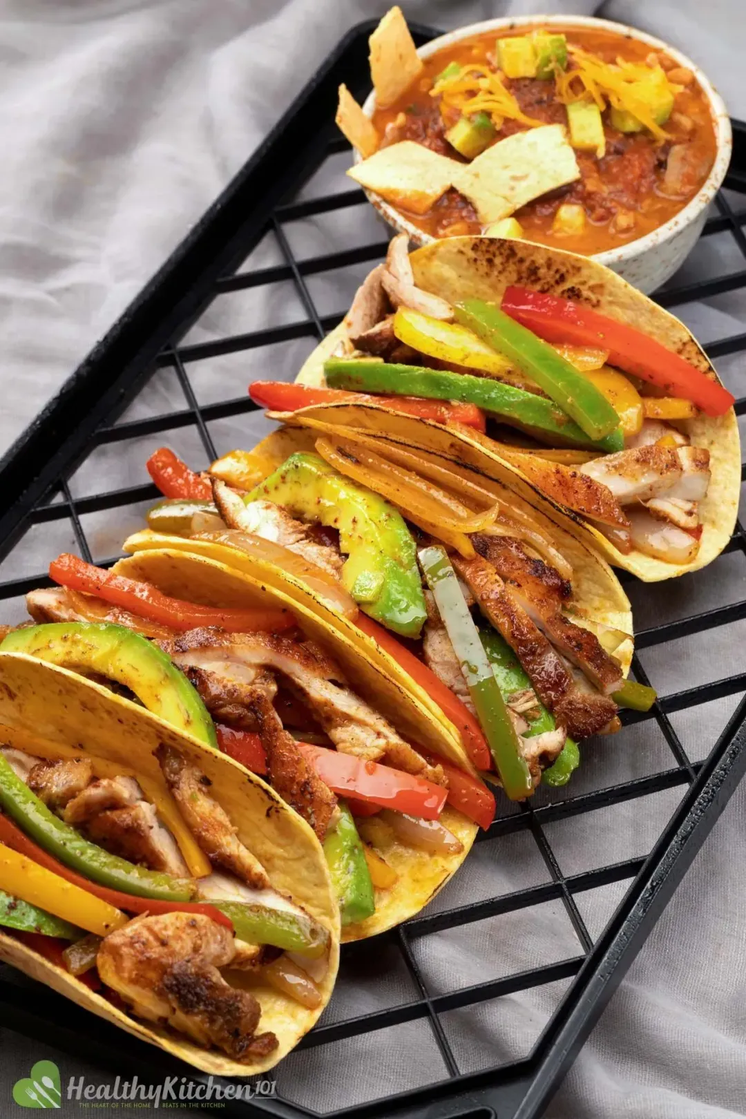 Four Chicken Fajitas tacos and a bowl of tortilla soup placed on a rack