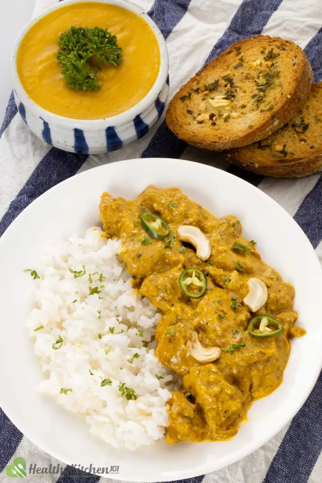 A chicken korma and rice plate next to garlic bread and pumpkin soup topped with parsley