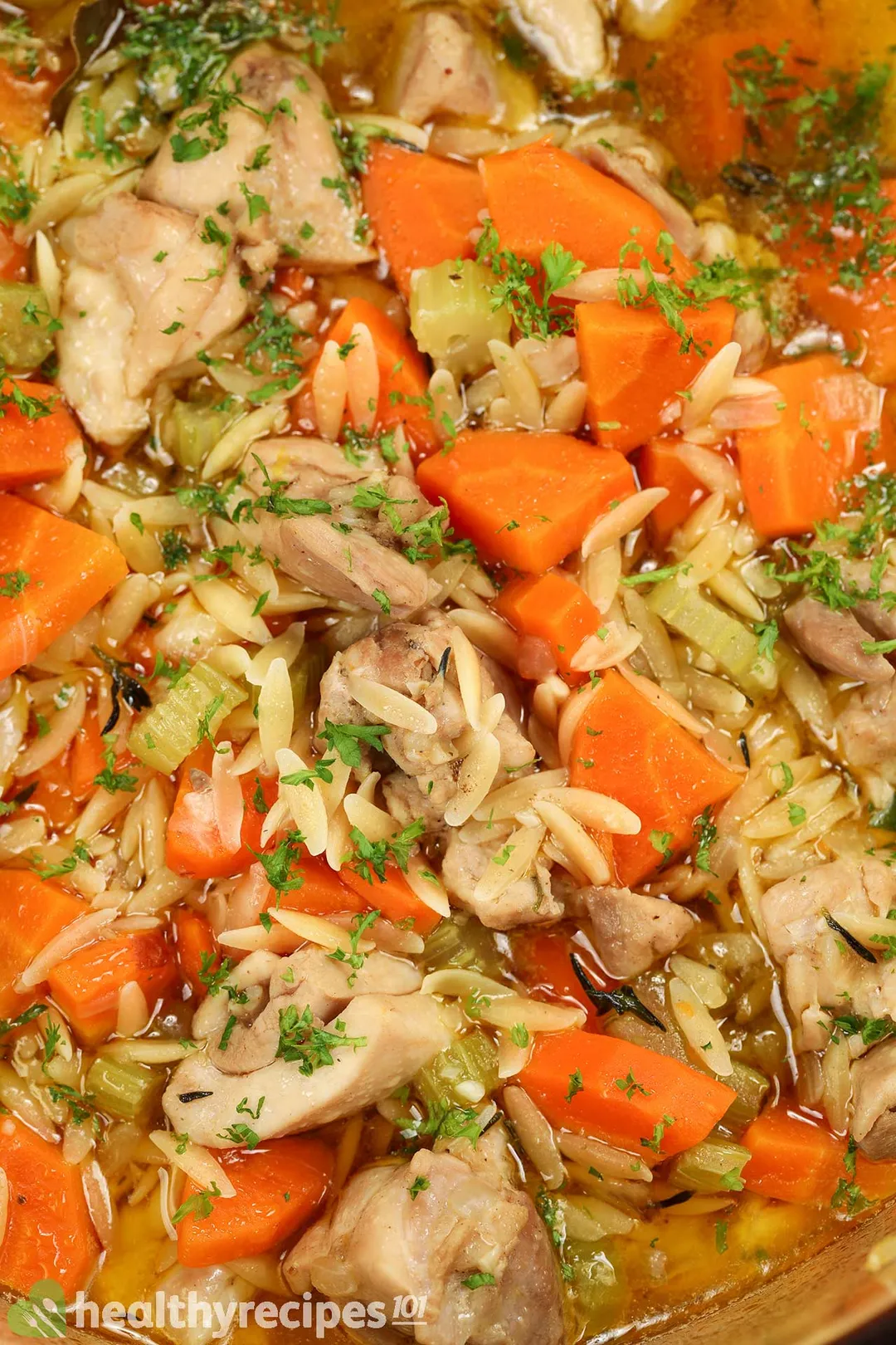 close shot of cooked chicken orzo soup with carrot cubes, chopped parsley on top