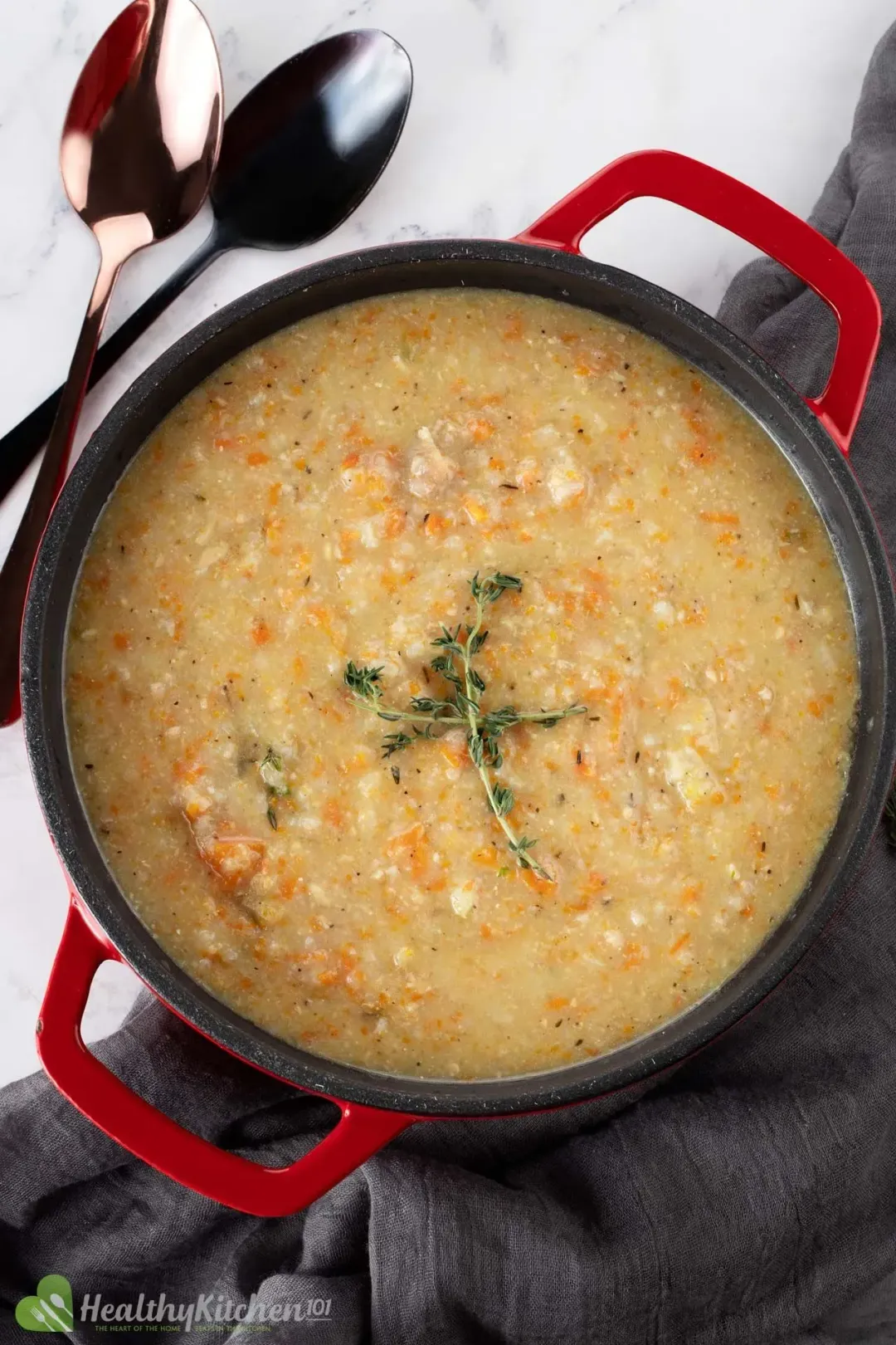 A pot of of chicken and rice soup with red handles and spoons on the side