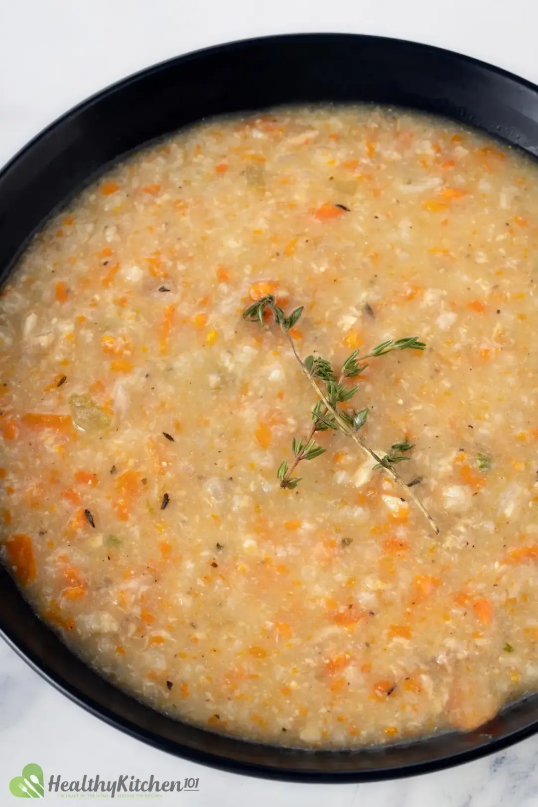A bowl of chicken and rice soup filled with carrot pieces and topped with rosemary sprigs