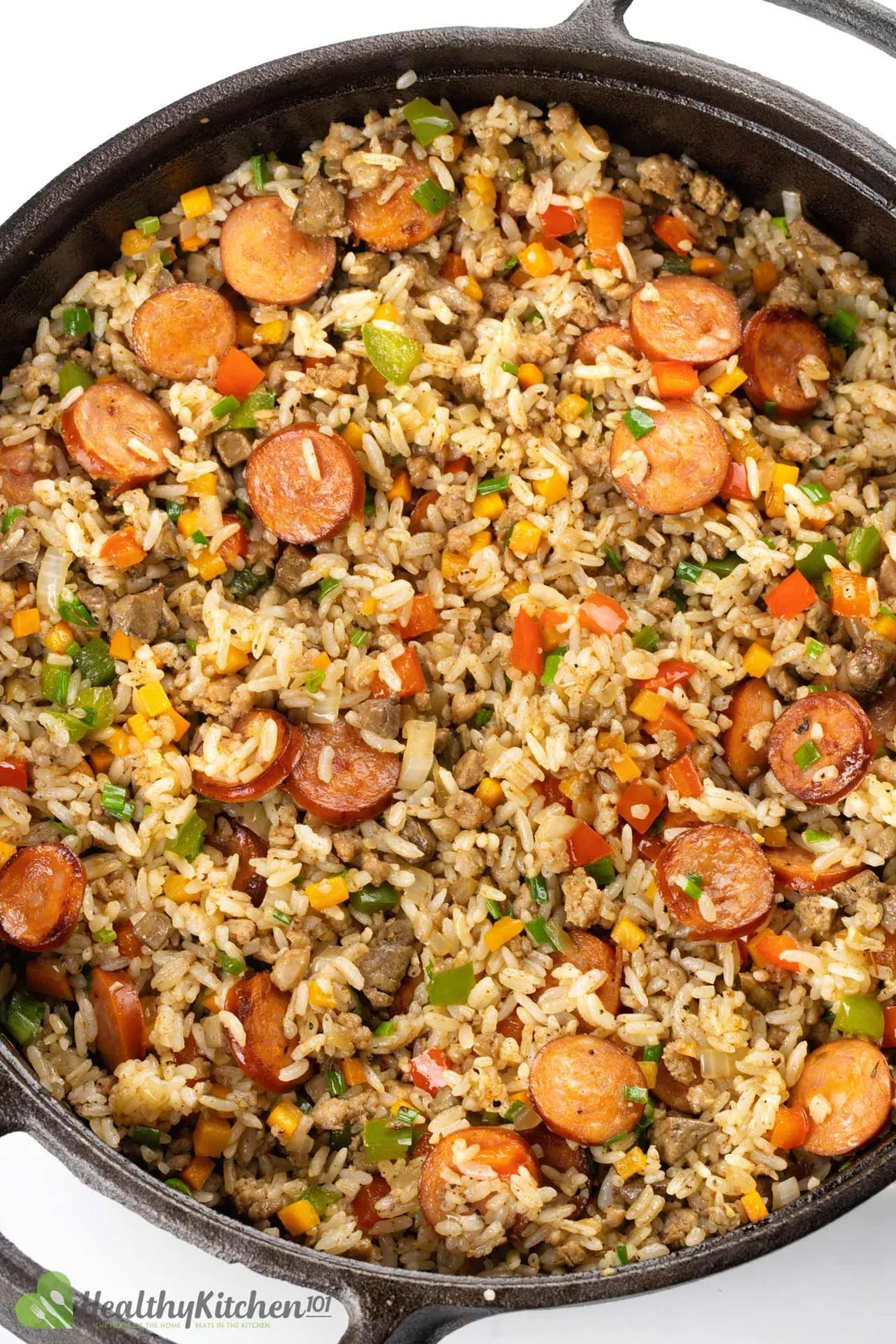 a cast iron skillet of cooked rice with sliced sausage and chicken, chopped pepper, carrot