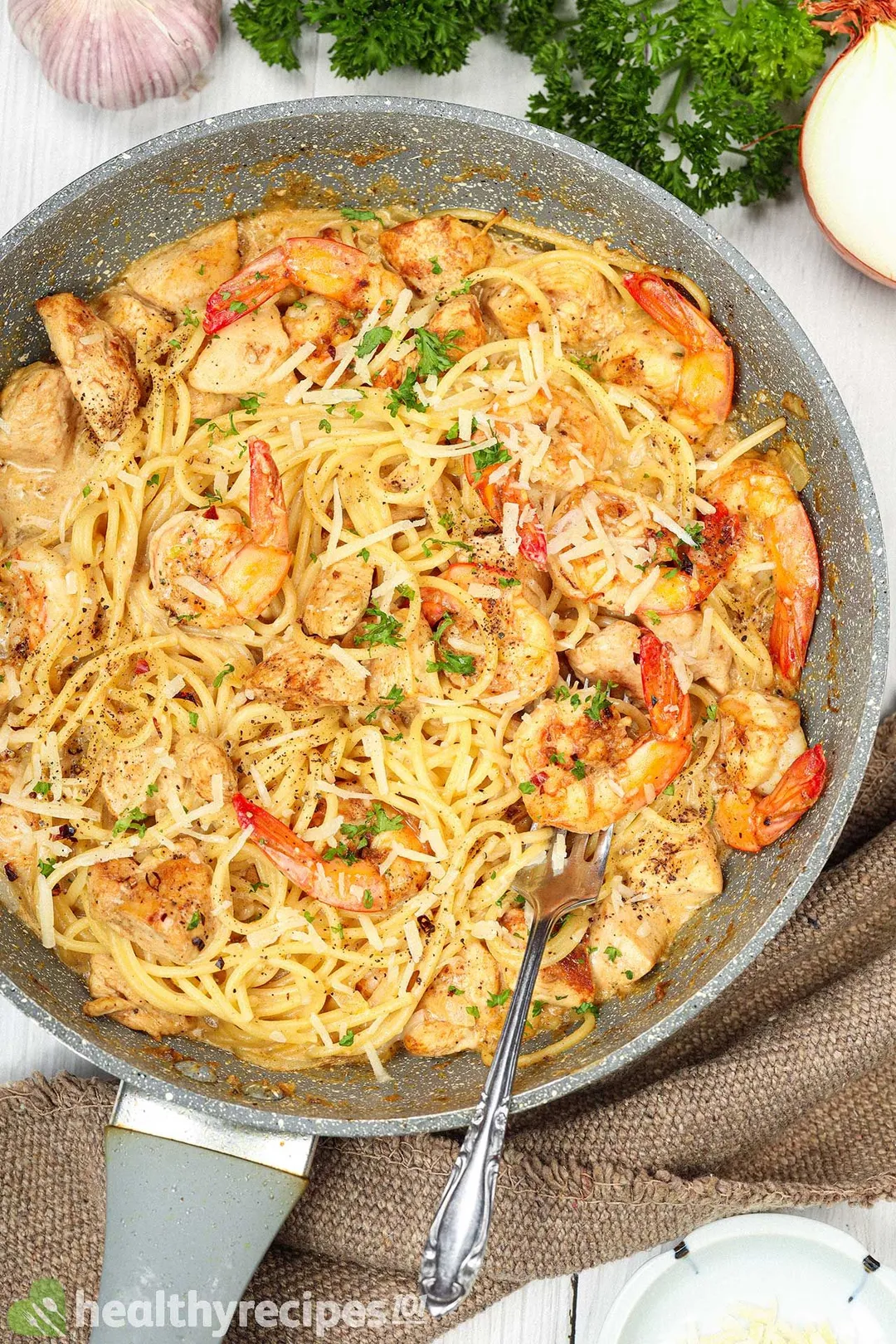 A skillet of cheesy spaghetti, cooked shrimp, and chicken chunks with a metal fork digging in