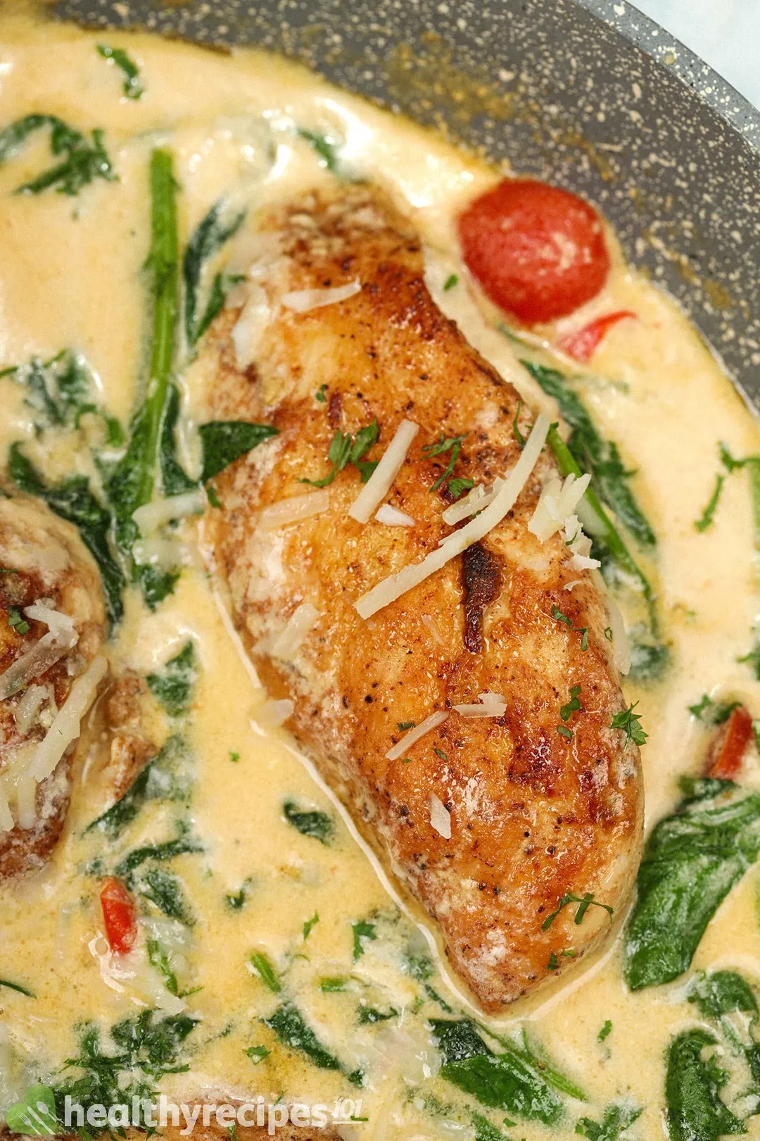 close-up shot of cooked chicken breast with spinach, tomato and cheese in a skillet