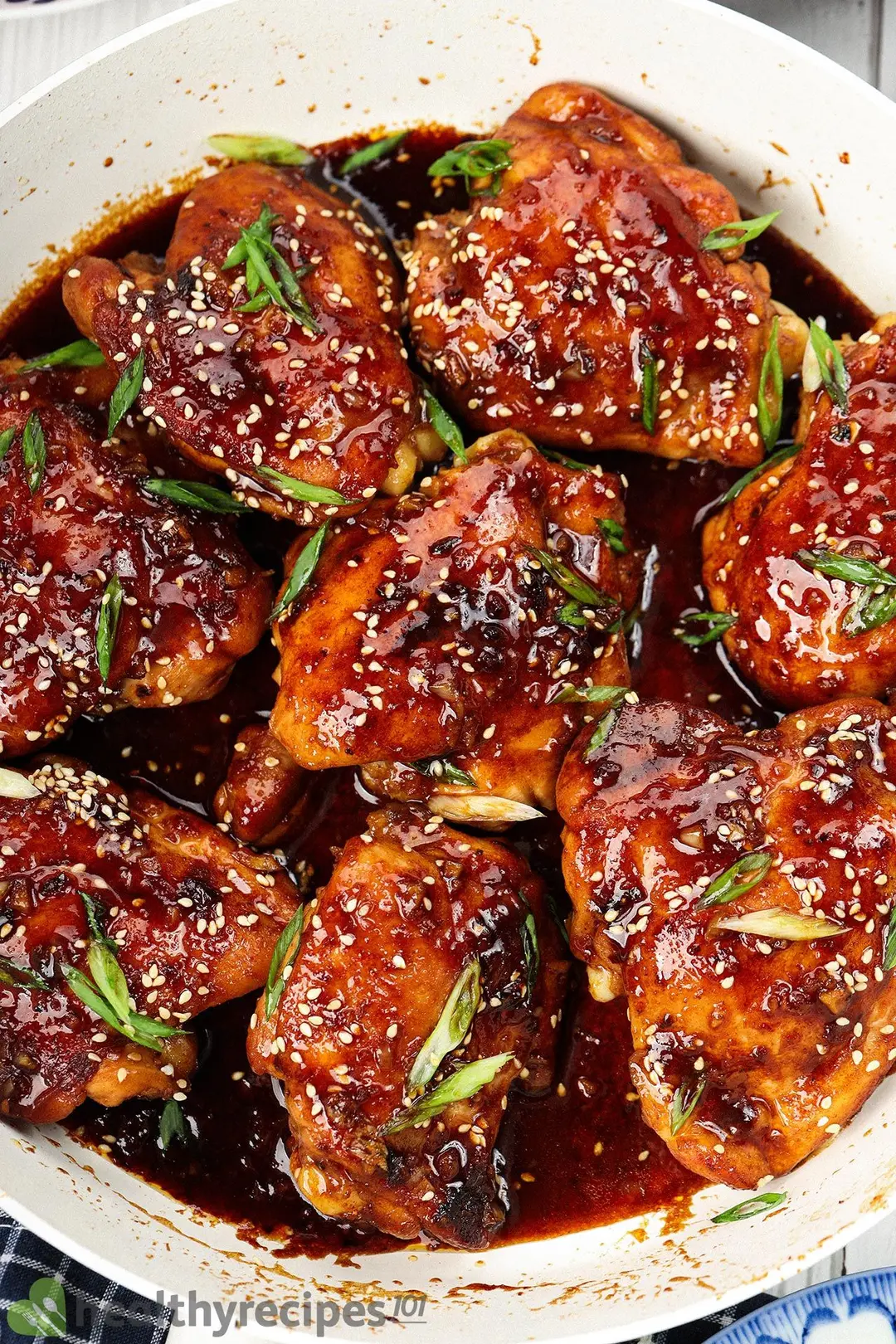 a non-stick skillet of cooked chicken thighs with sauce decorated with chopped scallion and sesame seeds