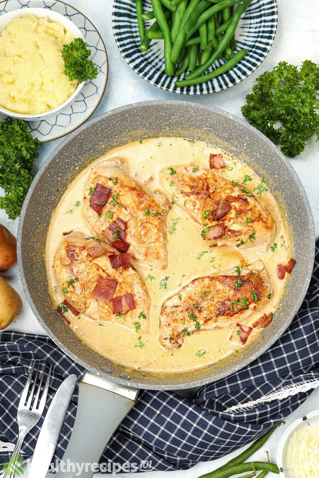 A large pan containing four pieces of cooked chicken breasts and small bacon pieces drenched in a pale yellow cream sauce