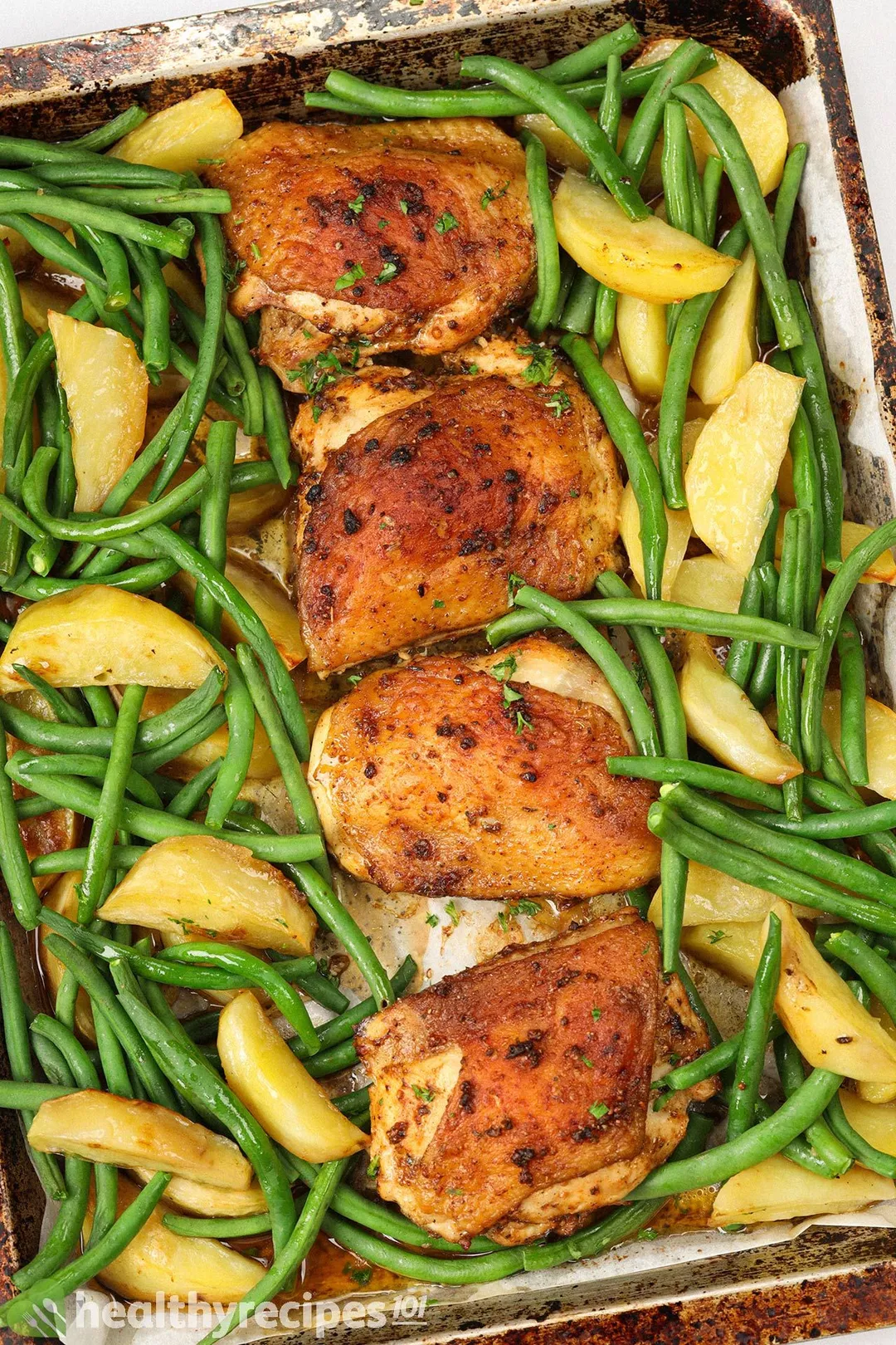 four baked chicken thighs with green beans and wedge potato on a baking tray