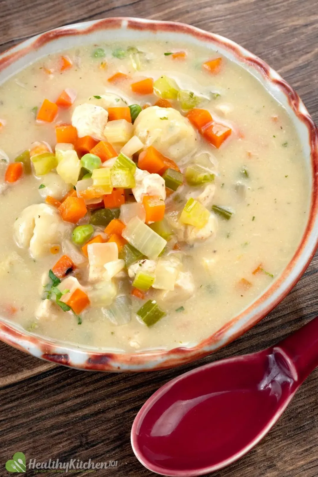 A bowl of Chicken and Dumplings soup topped with diced vegetables and a red spoon.