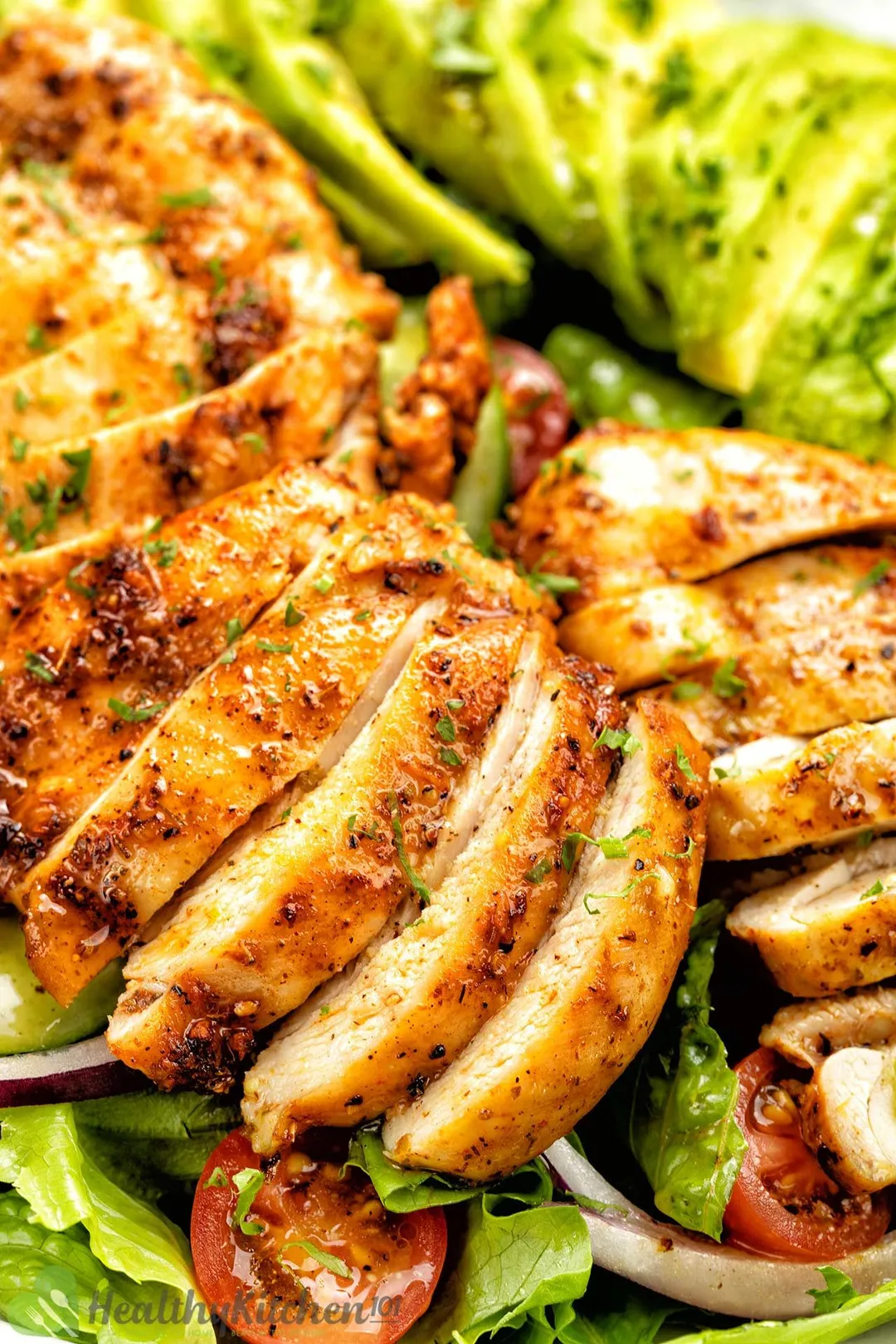 close-up shot of sliced grilled chicken breast bed on lettuce, half tomatoes