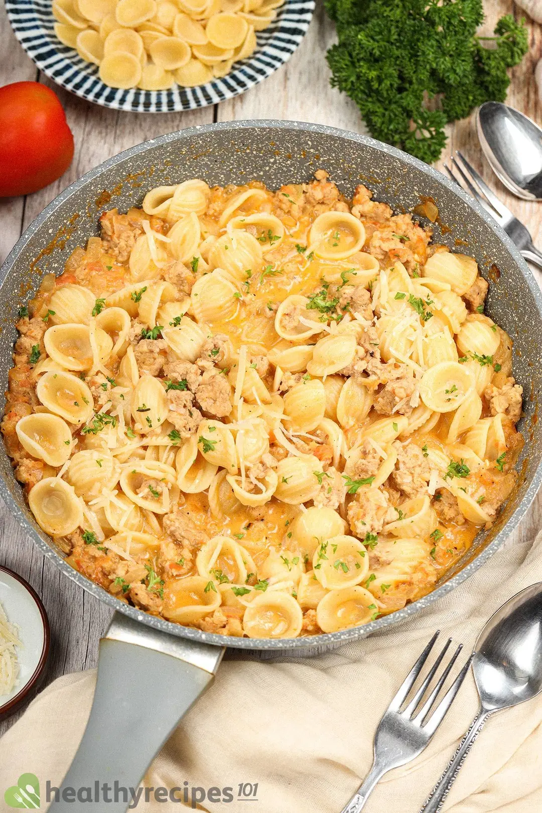 Ground chicken pasta in a pan alongside utensils and raw pasta