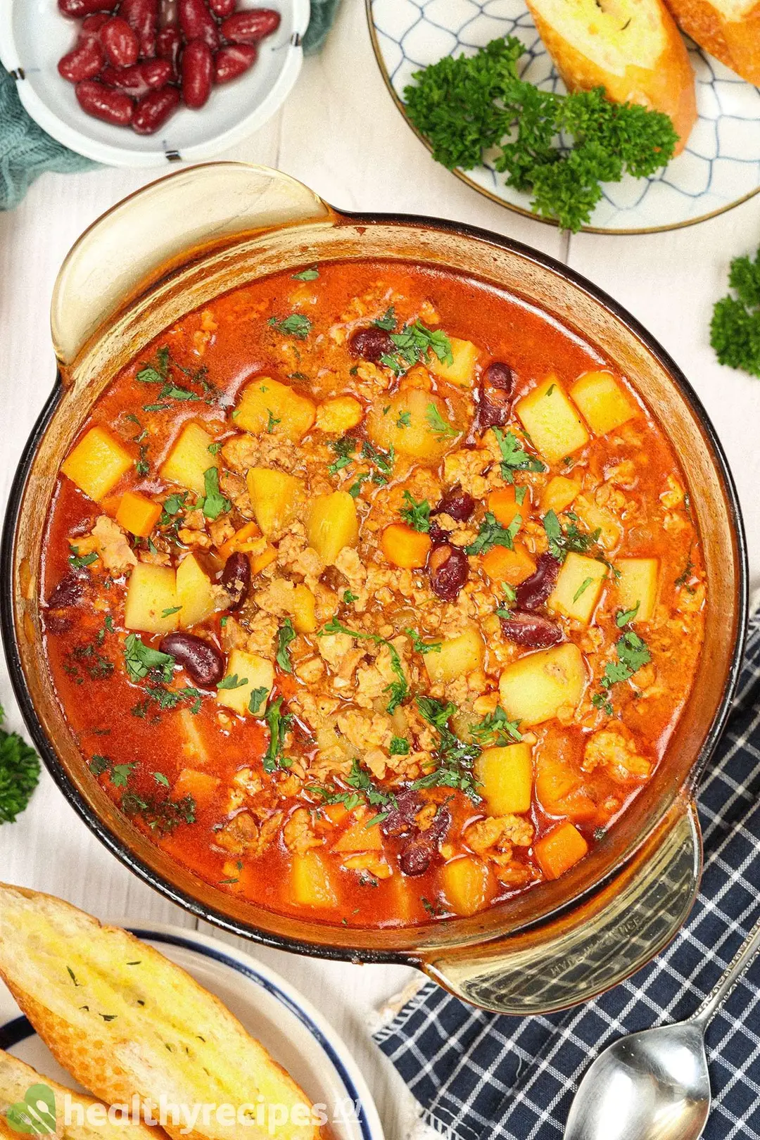 A large pot of ground chicken soup filled to the brim with cubed carrots, cubed potatoes, and ground chicken, garnished with chopped parsley