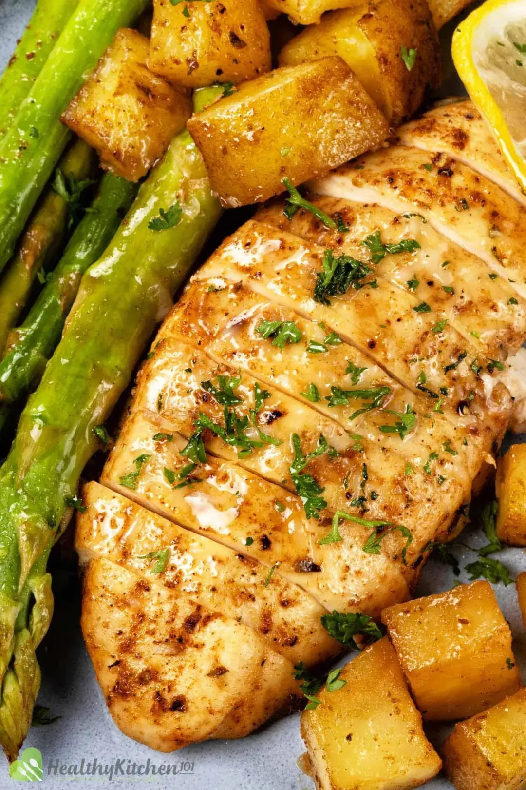 A piece of baked chicken breast surrounded by potato cubes and asparagus