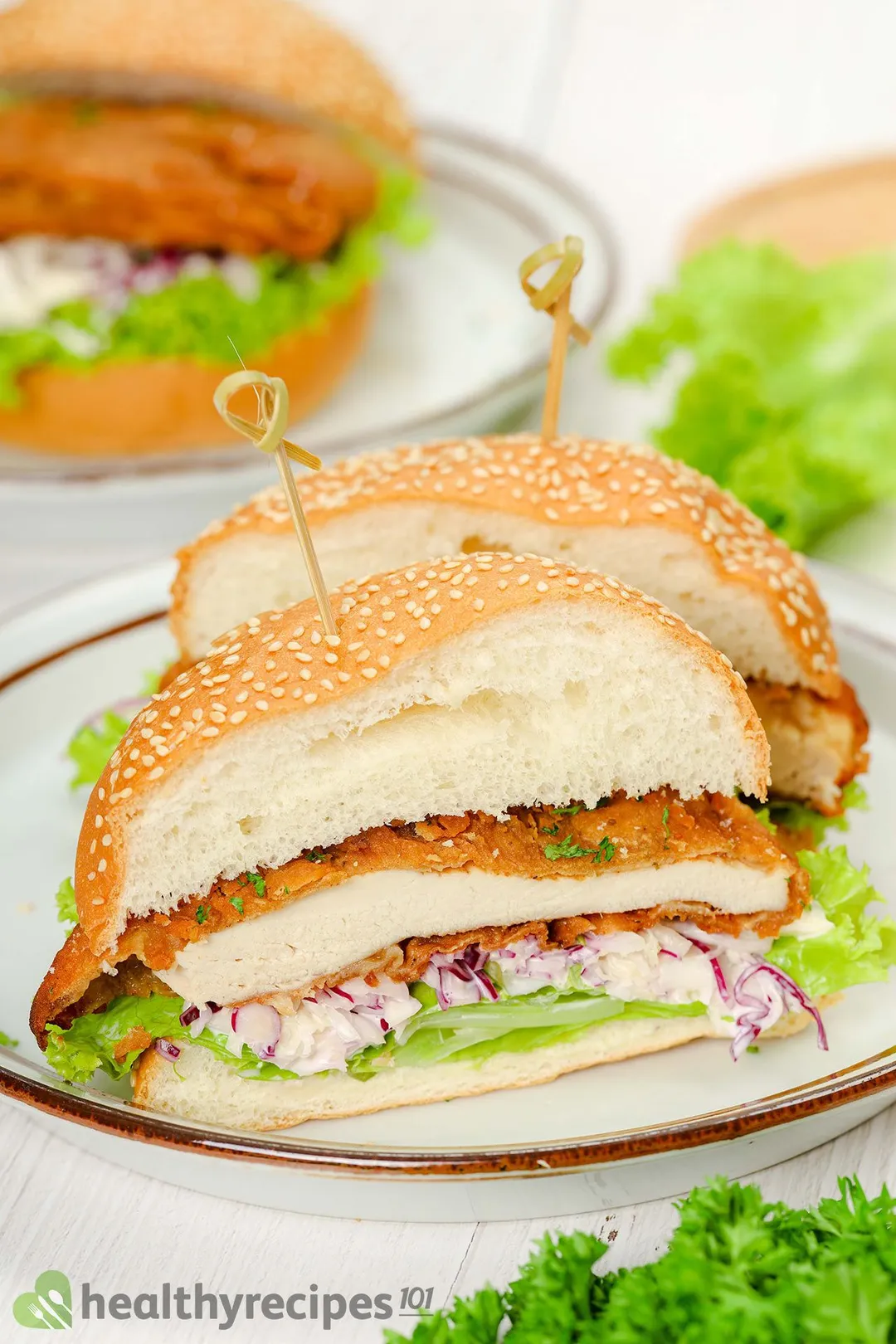 two half of cooked chicken burger with shredded cabbage and lettuce on a plate