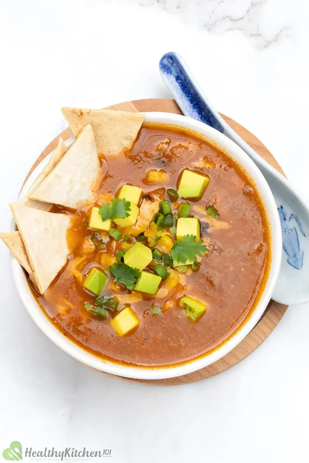 A bowl of chicken tortilla soup placed on a small plate and next to a spoon