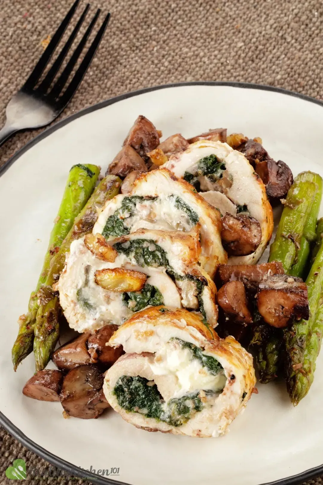 A plate of Stuffed Chicken Breast placed on a bed of asparagus.