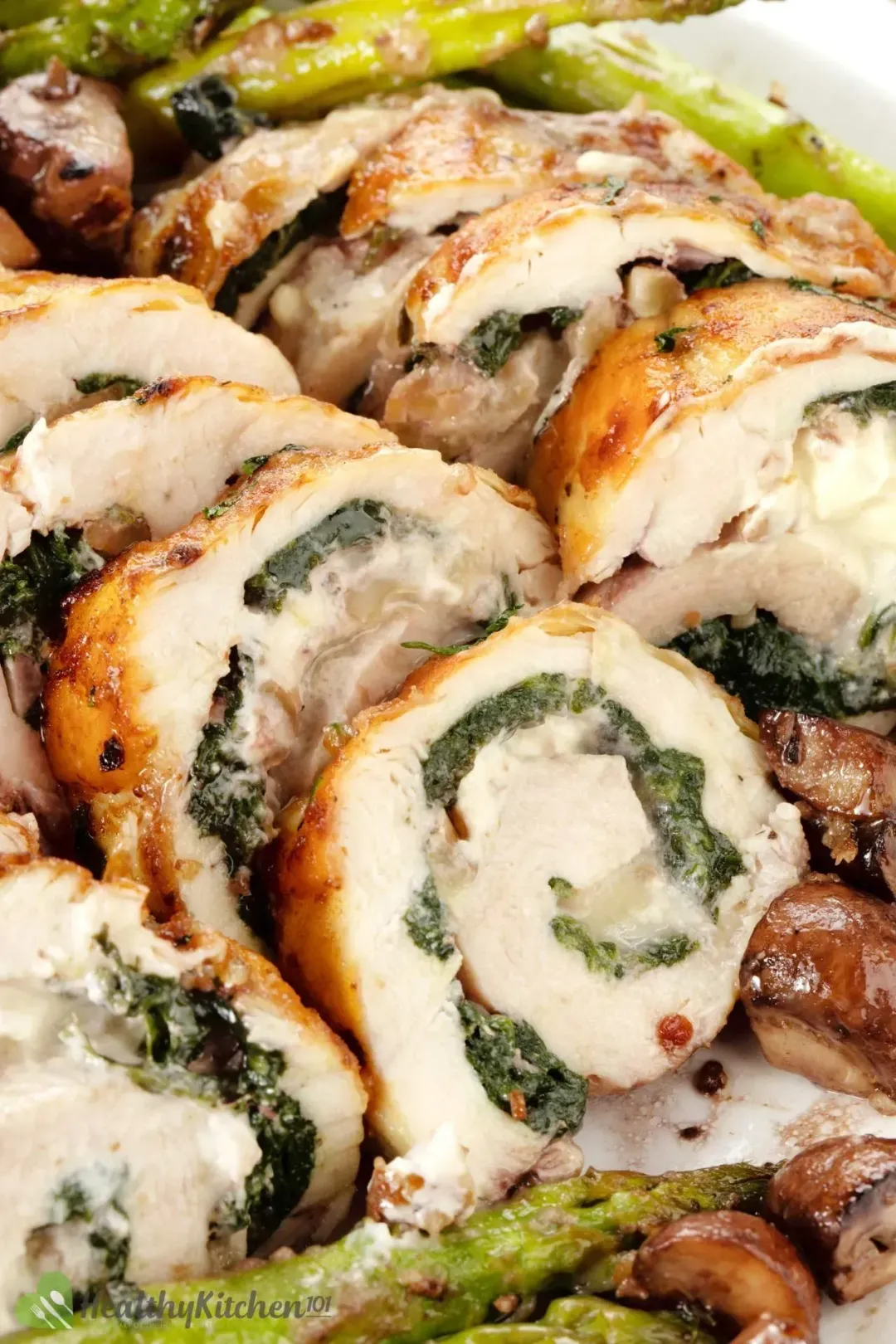 A close-up shot of chicken rolls stuffed with spinach and laid near asparagus.