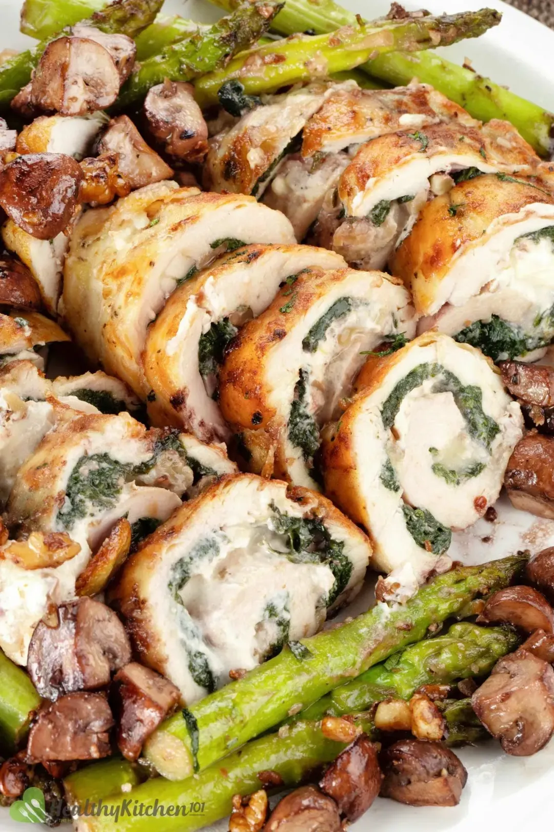 Rolls of chicken breasts stuffed with spinach laid on a bed of aspragus and brown mushrooms.