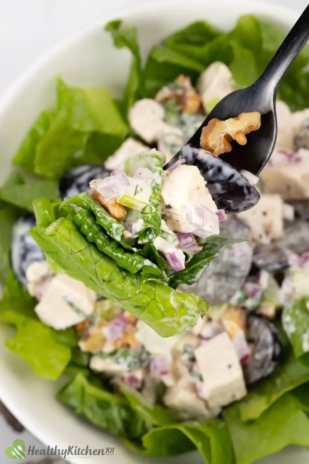 A fork holding lettuce, halved grapes, walnuts, and fruits covered in white dressing hovering over a salad bowl