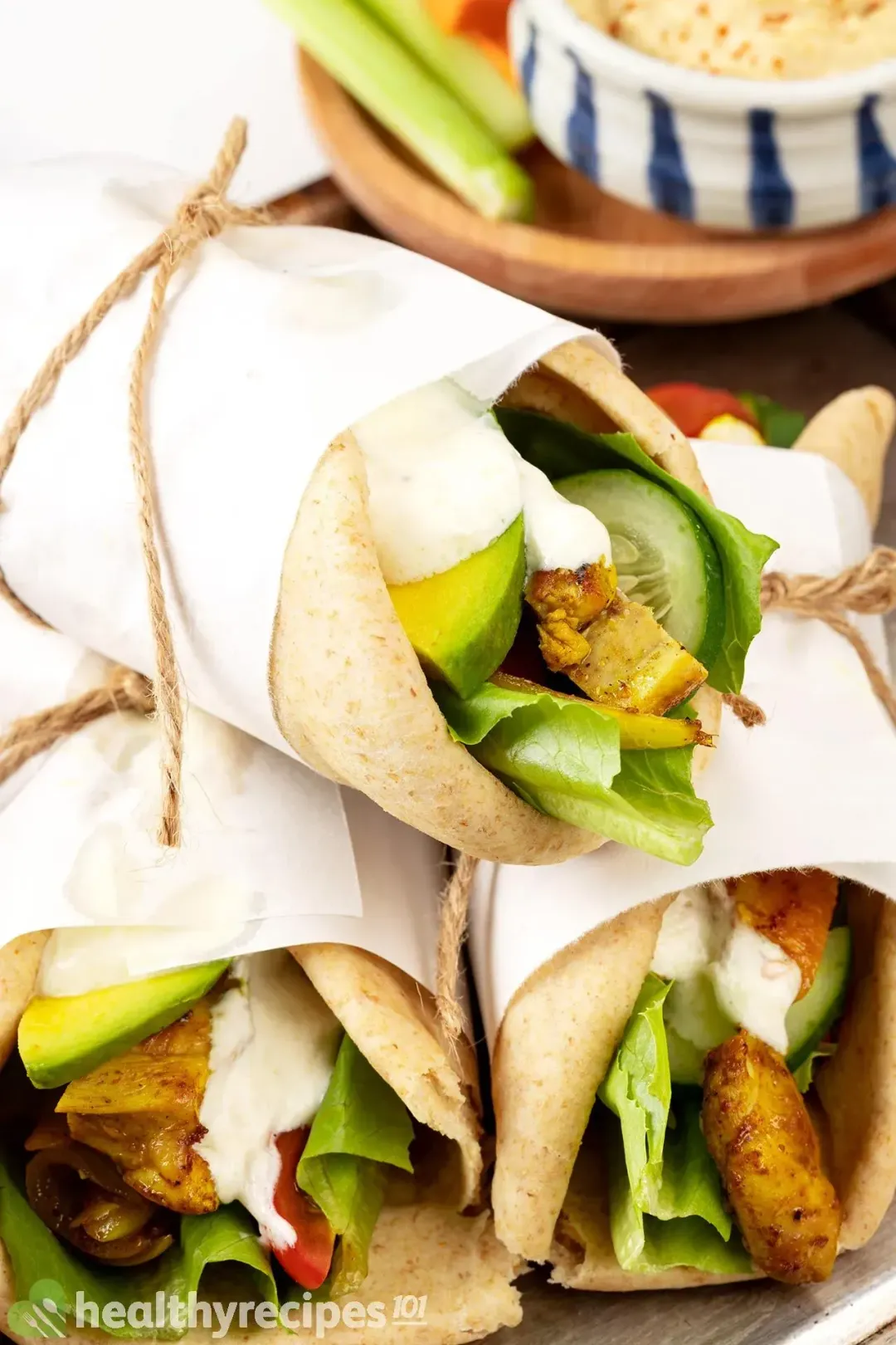 A close-up shot of a stack of three chicken shawarma pita wraps, with vegetables and meat showing