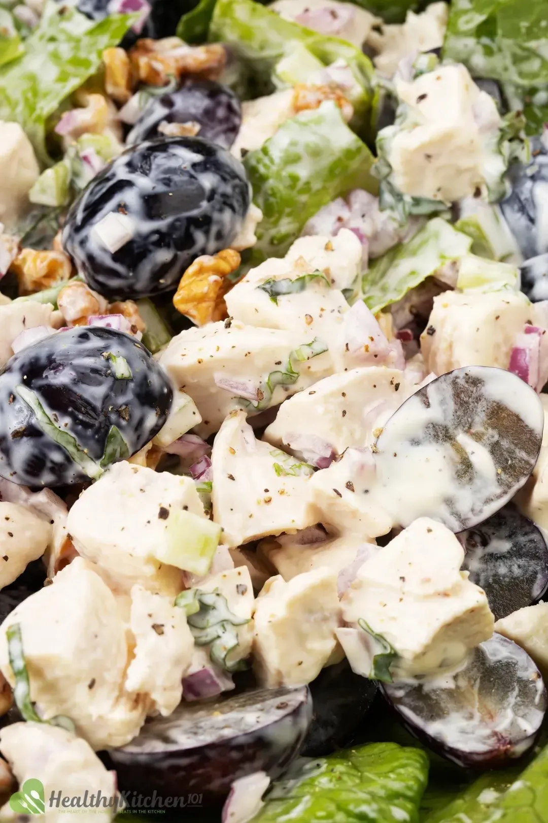 A fork holding lettuce, halved grapes, walnuts, and fruits covered in white dressing hovering over a salad bowl