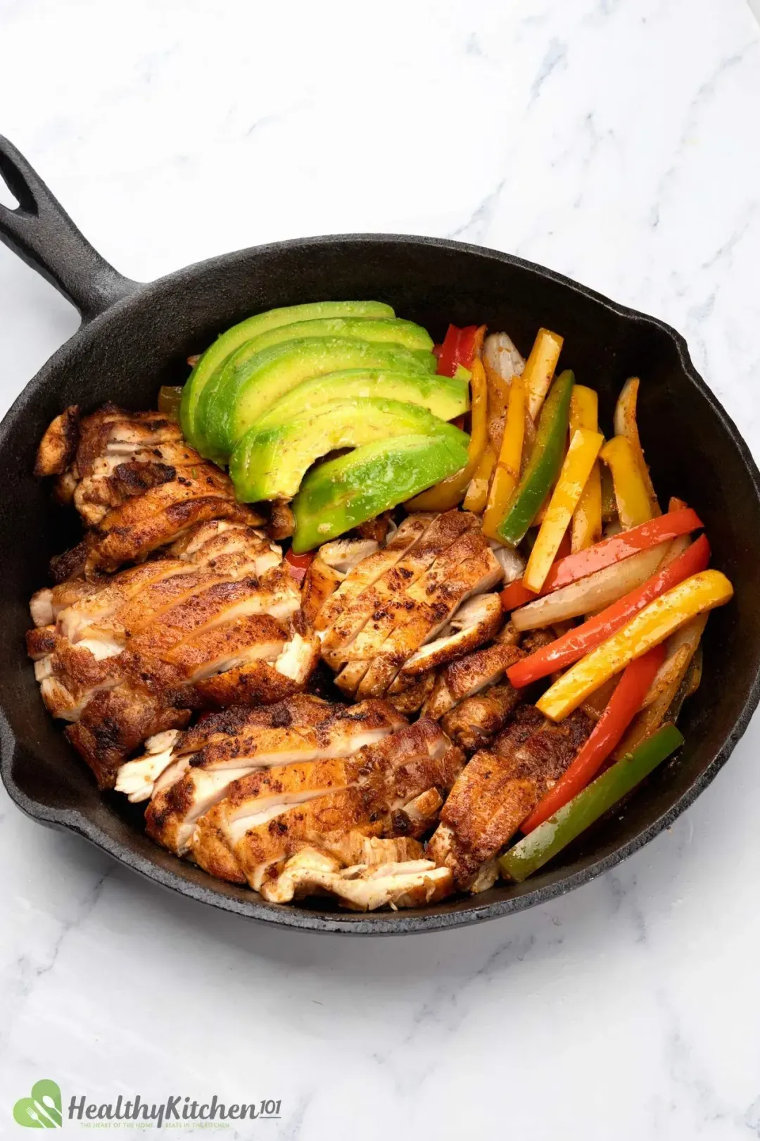 A skillet filled with pan seared chicken slices, bell pepper sticks, and avocado slices
