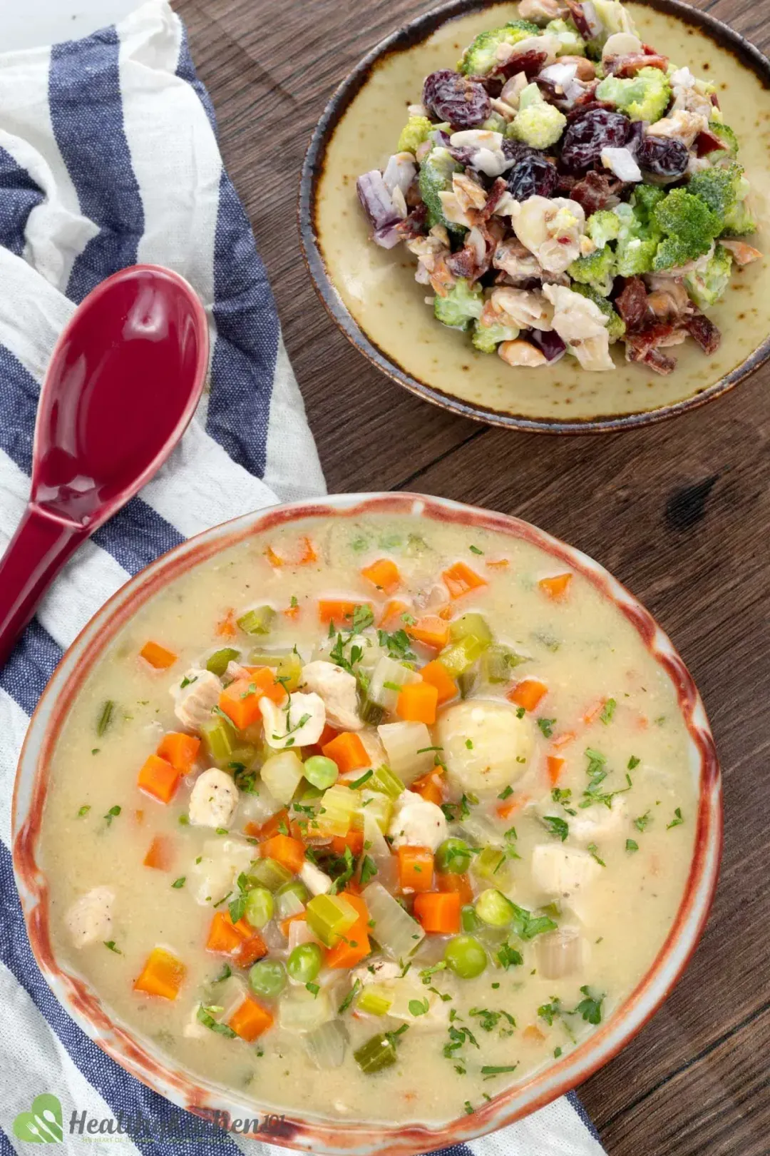 A bowl of Chicken And Dumplings placed next to a dish of sauteed vegetables and a red spoon.