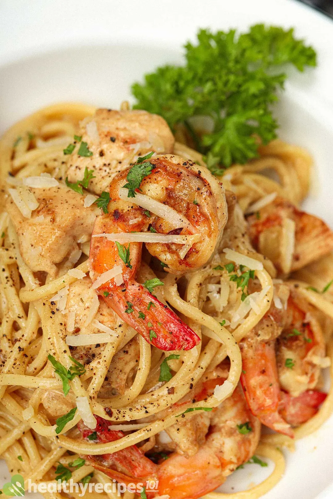 A close-up shot of a chicken and shrimp alfredo plate garnished with a parsley sprig