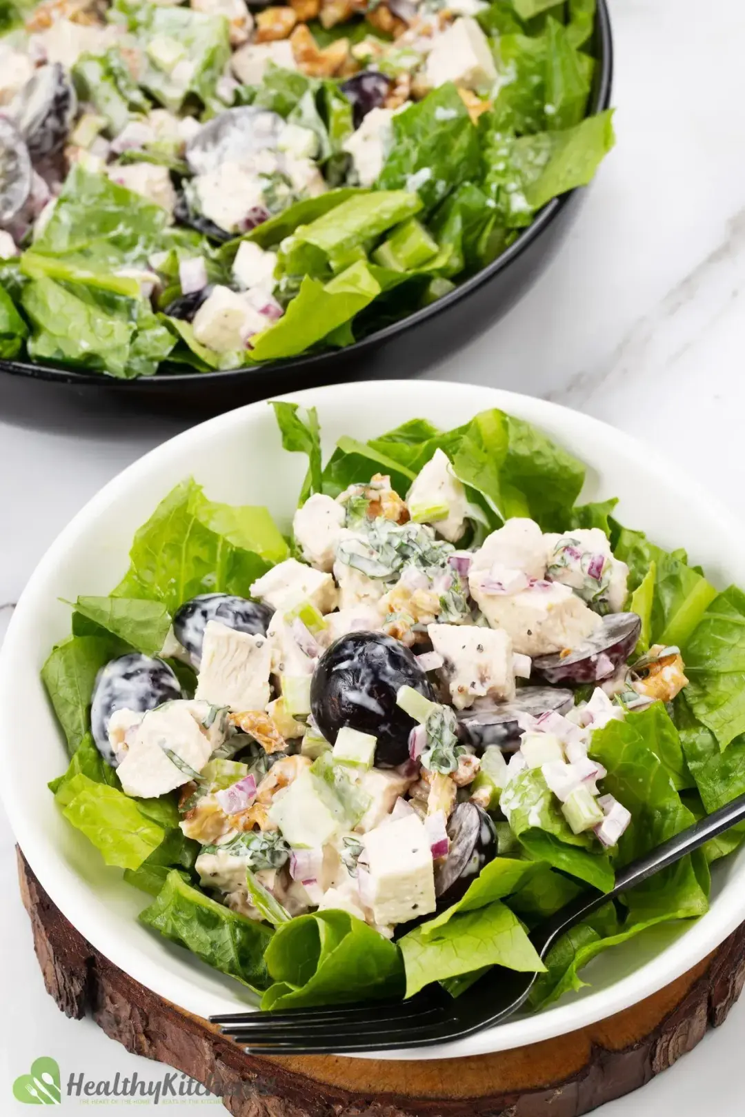 Two plates of waldorf chicken salad with chopped fruits, celery, halved grapes, and romaine lettuce with a black fork