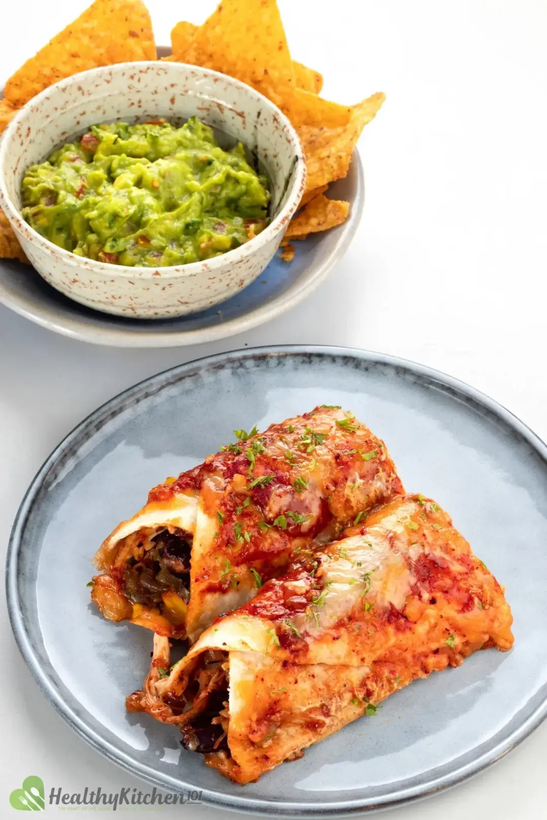 Two golden enchiladas with cheese and tomato sauce next to chips and guacamole