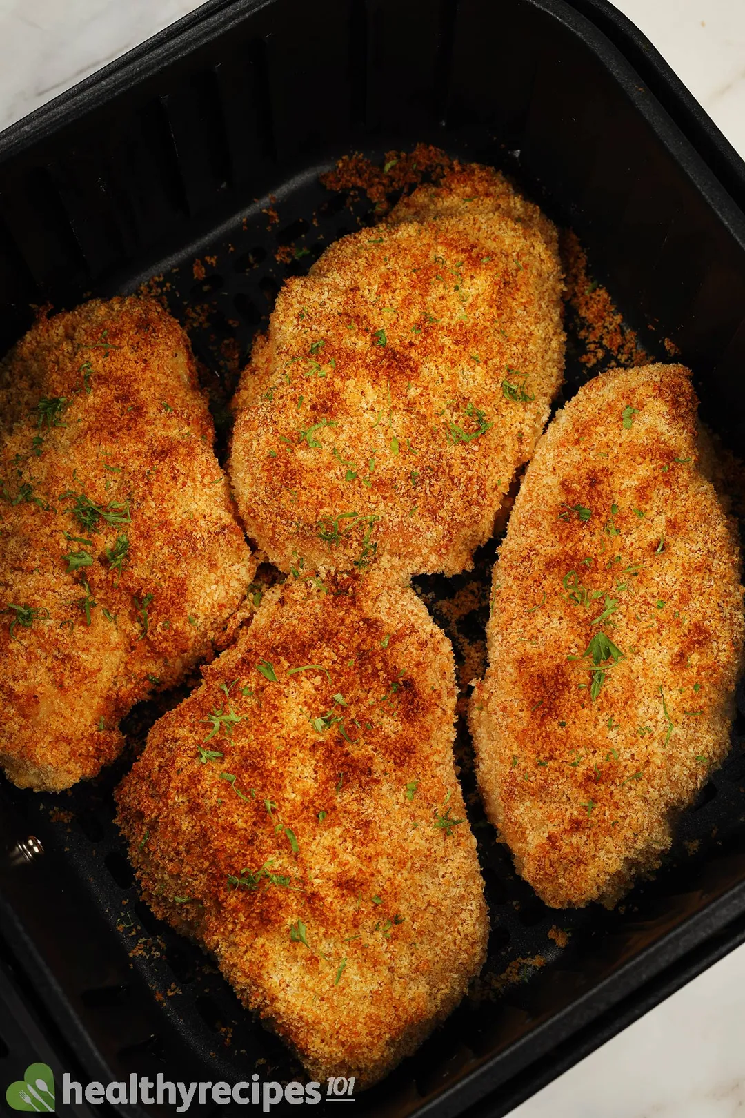 four cooked chicken breasts in an air fryer basket