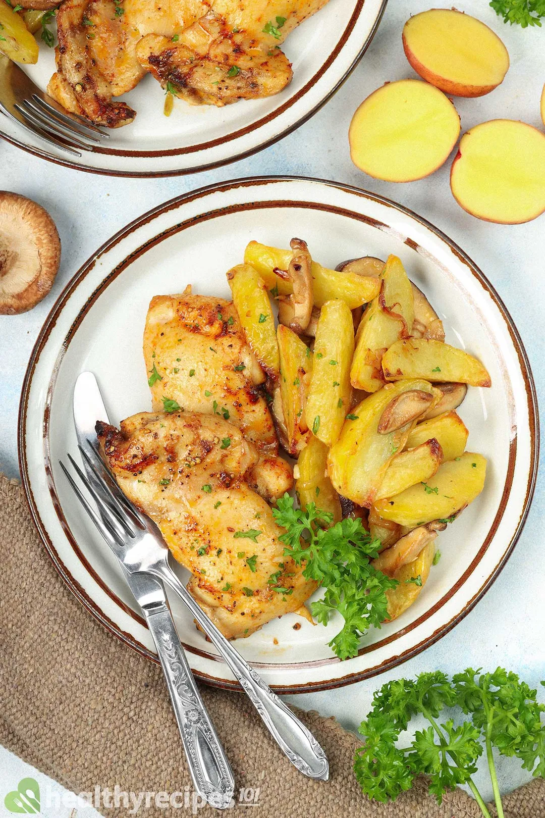 a plate of broiled chicken thighs with cooked potato wedge decorated with fork spoon half potatoes parsley