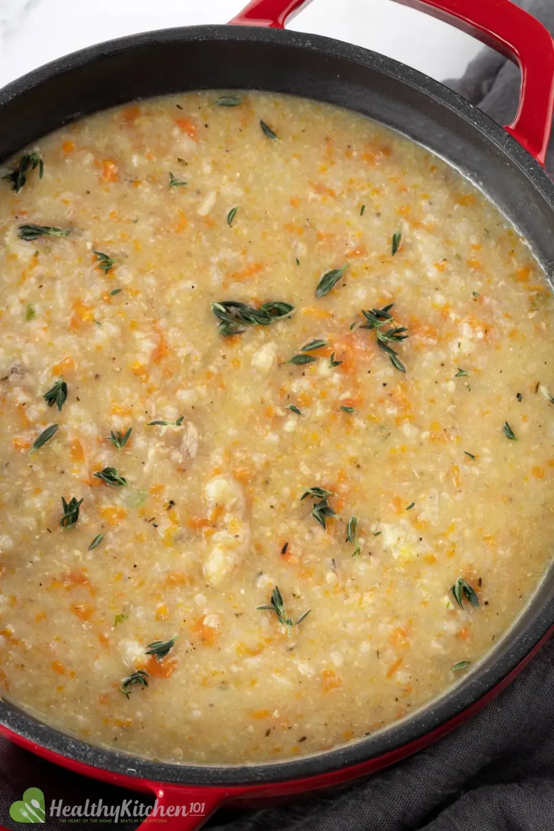 A pot of of chicken and rice soup with red handles and spoons on the side