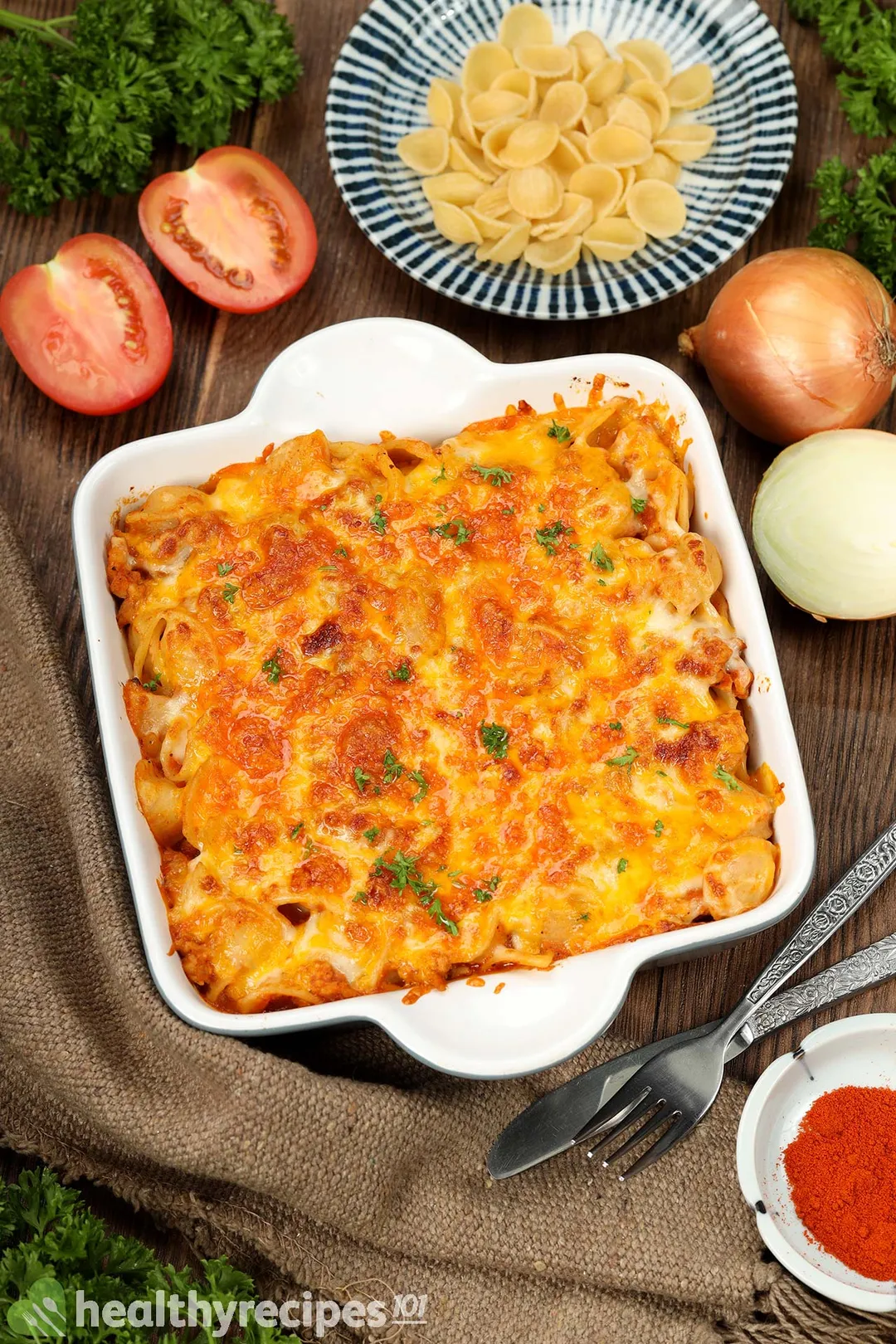 a casserole of ground chicken and pasta decorated with half tomatoes, onion and a plate of uncooked pasta