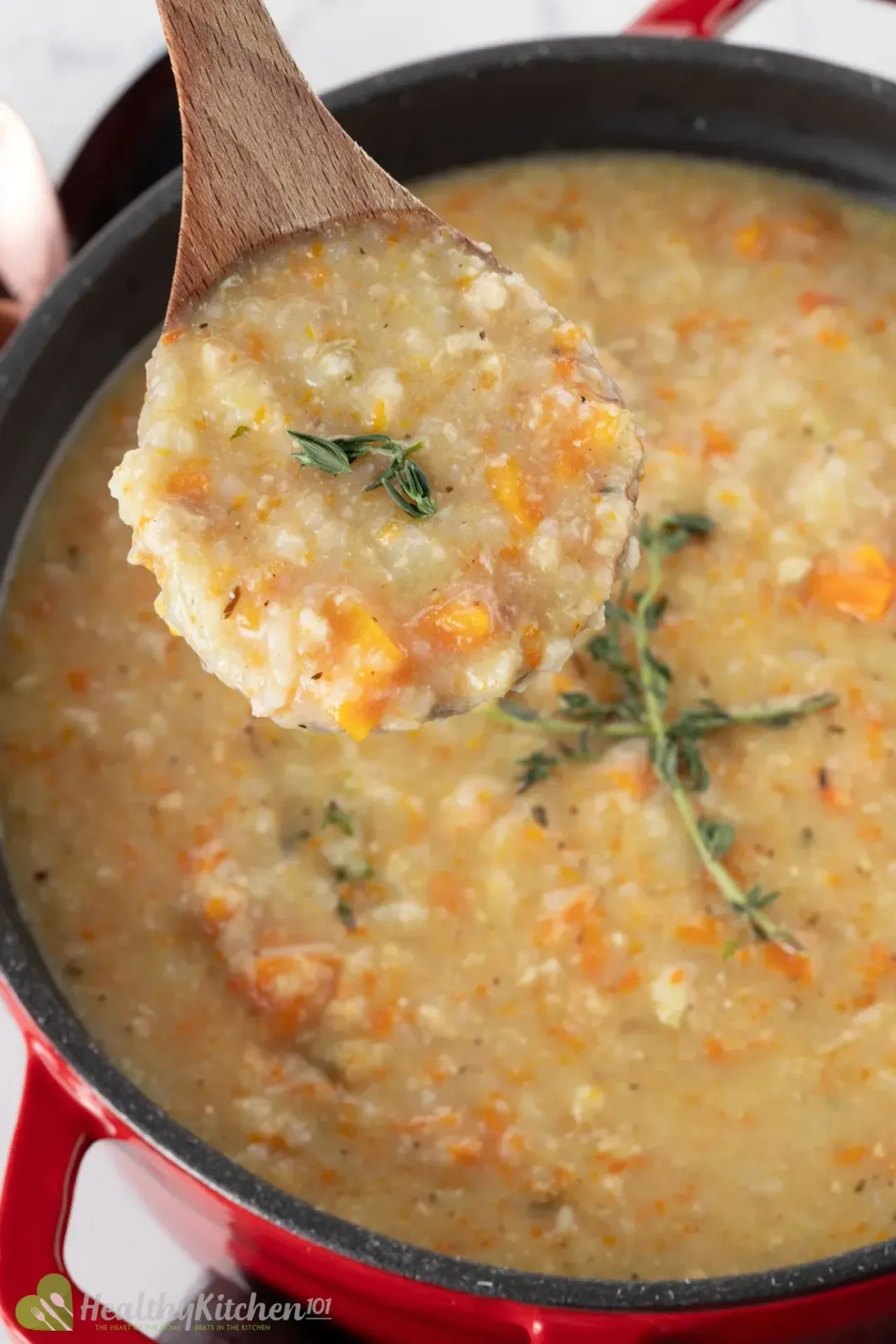 A wooden ladle holding chicken and rice soup over a red pot of soup topped with rosemary sprigs