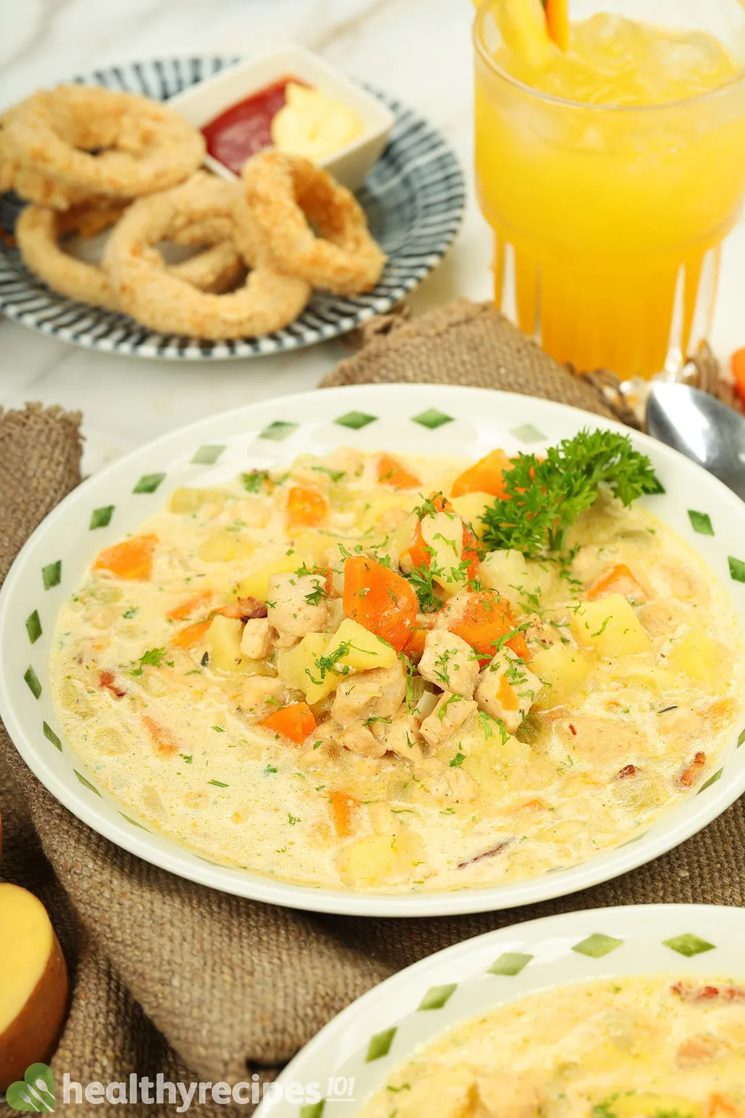 front shot of a plate of chicken potato soup and a plate of onion rings, a glass of yellow juice