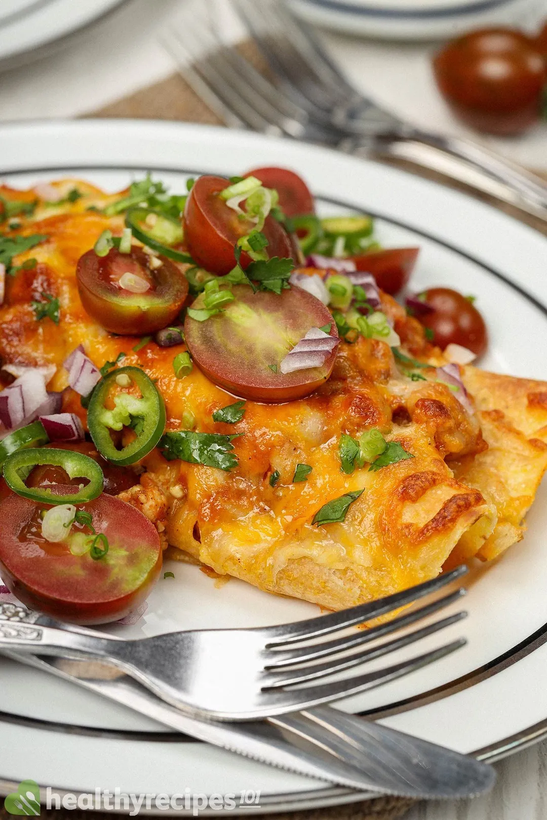 a plate of cooked chicken enchiladas with half tomatoes, slices jalapeno on top