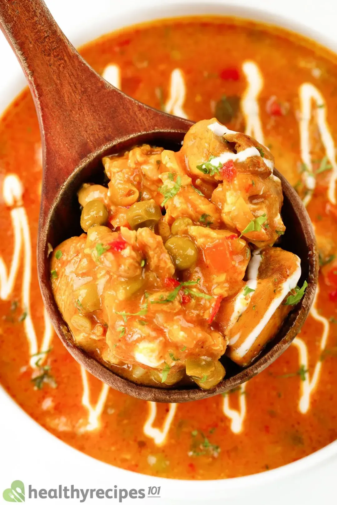 close-up shot of a wooden spoon of cooked cubed chicken breast with a bowl of red sauce in background