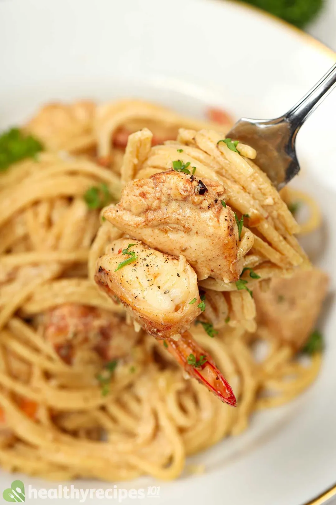 A close-up picture of a fork holding some cheesy pasta, a cooked shrimp, and a chicken breast chunk